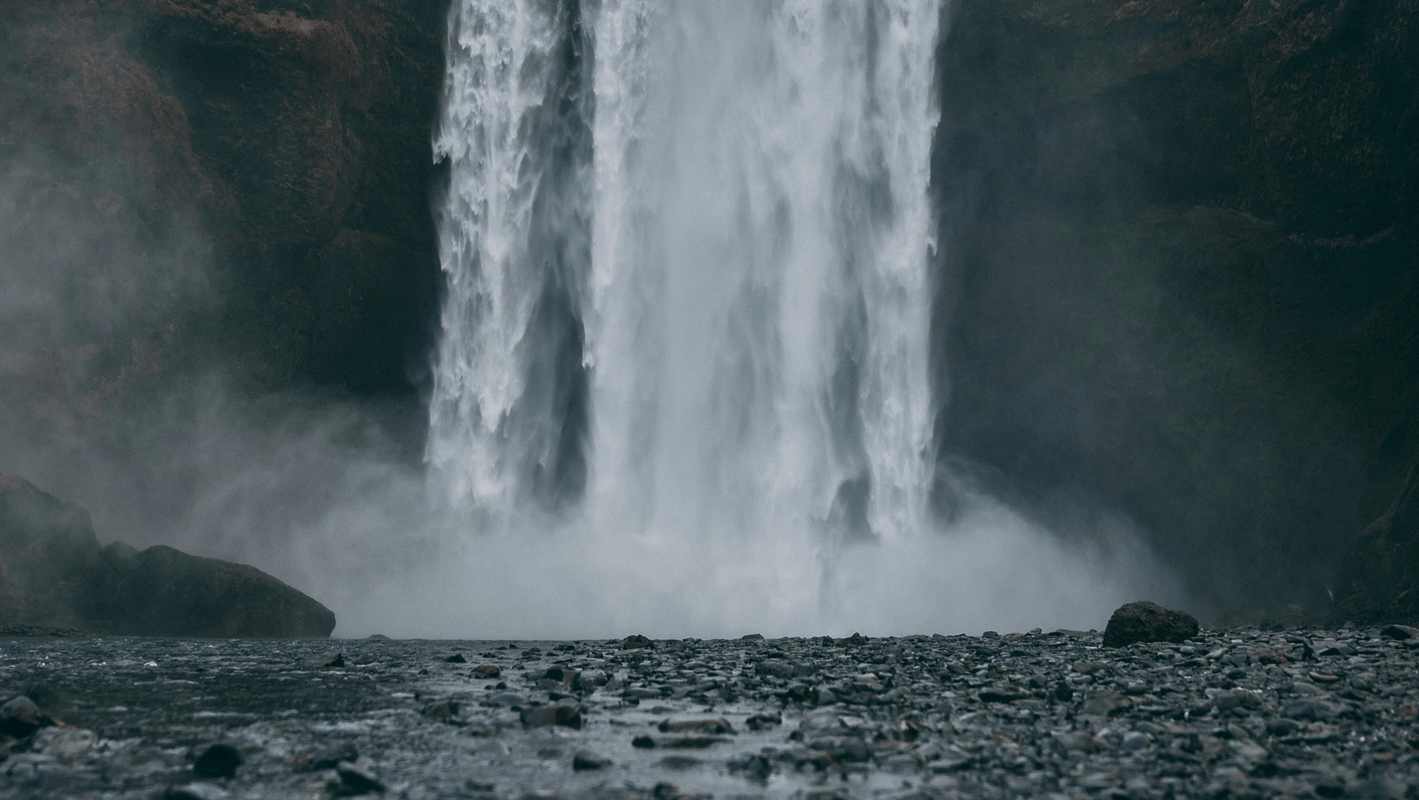 A dramatic waterfall cascading down a cliff, shrouded in mist, with rocky terrain in the foreground