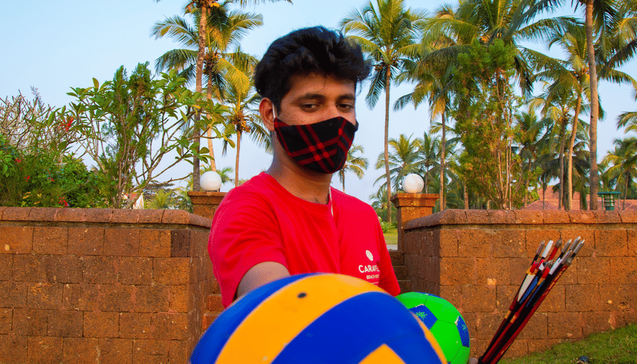 a person wearing a mask showing a volleyball with trees in the background - Caravela Beach Resort Goa