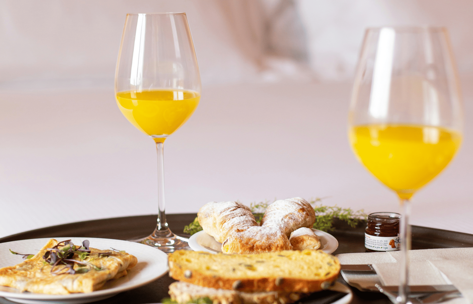 A room service breakfast tray with orange juice and an assortment of breakfast foods on a bed