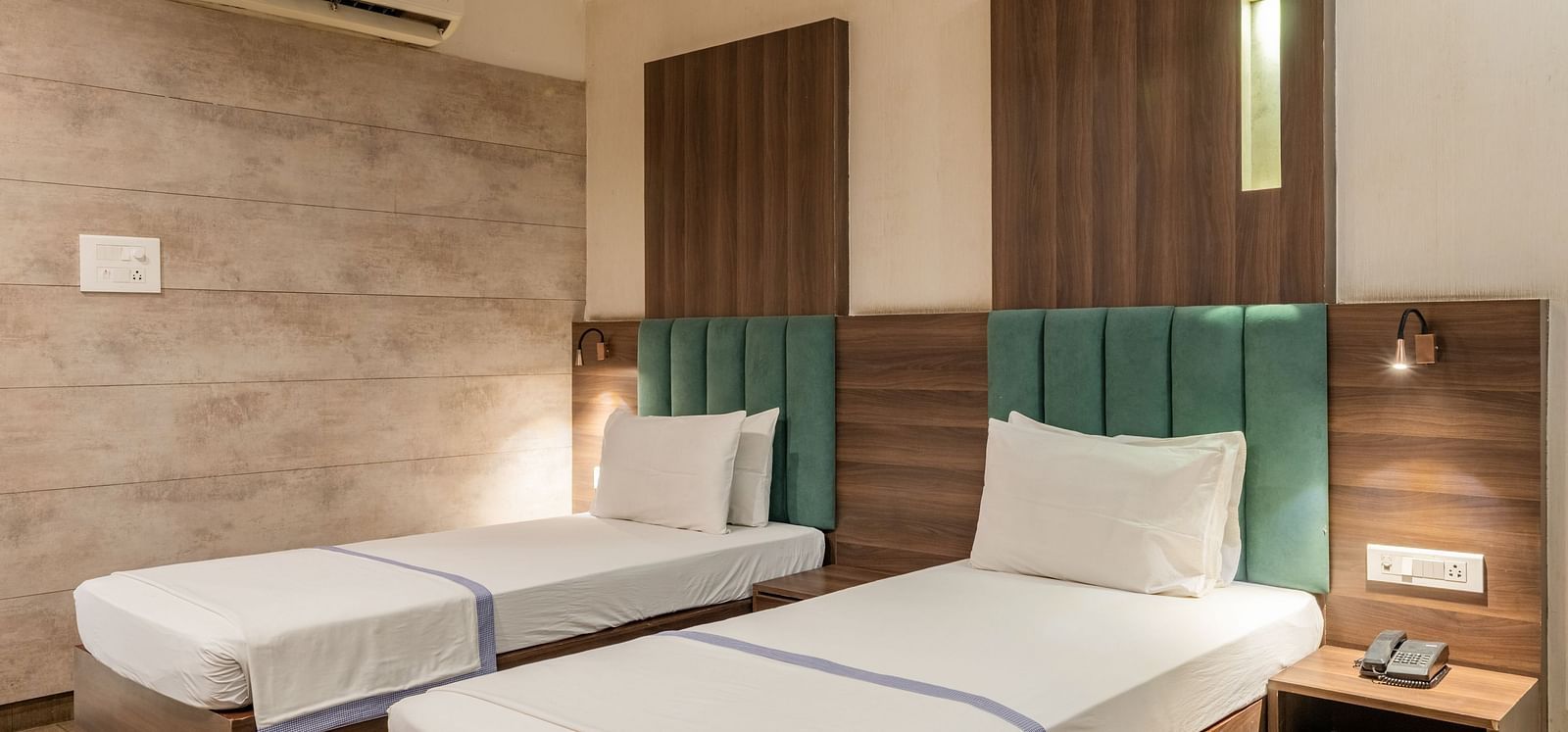 Twin beds with upholstered headboards and bedside tables in the Maharaja Deluxe Rooms of Hotel Highway King, Behror.