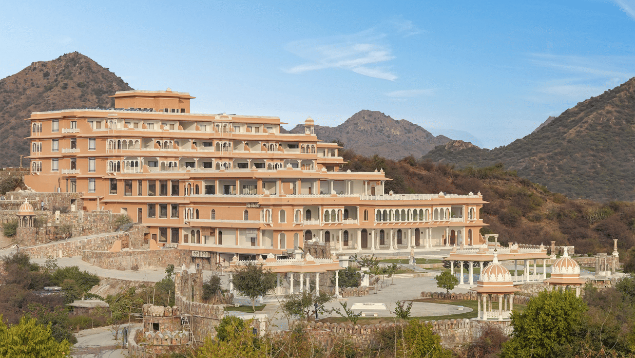 Location of Fateh Vilas by Fateh Collection with many trees in the foreground and mountains in the background