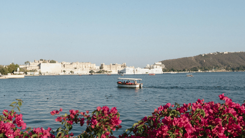 A boat sailing on the calm waters of Lake Pichola in Udaipur on a bright sunny day.