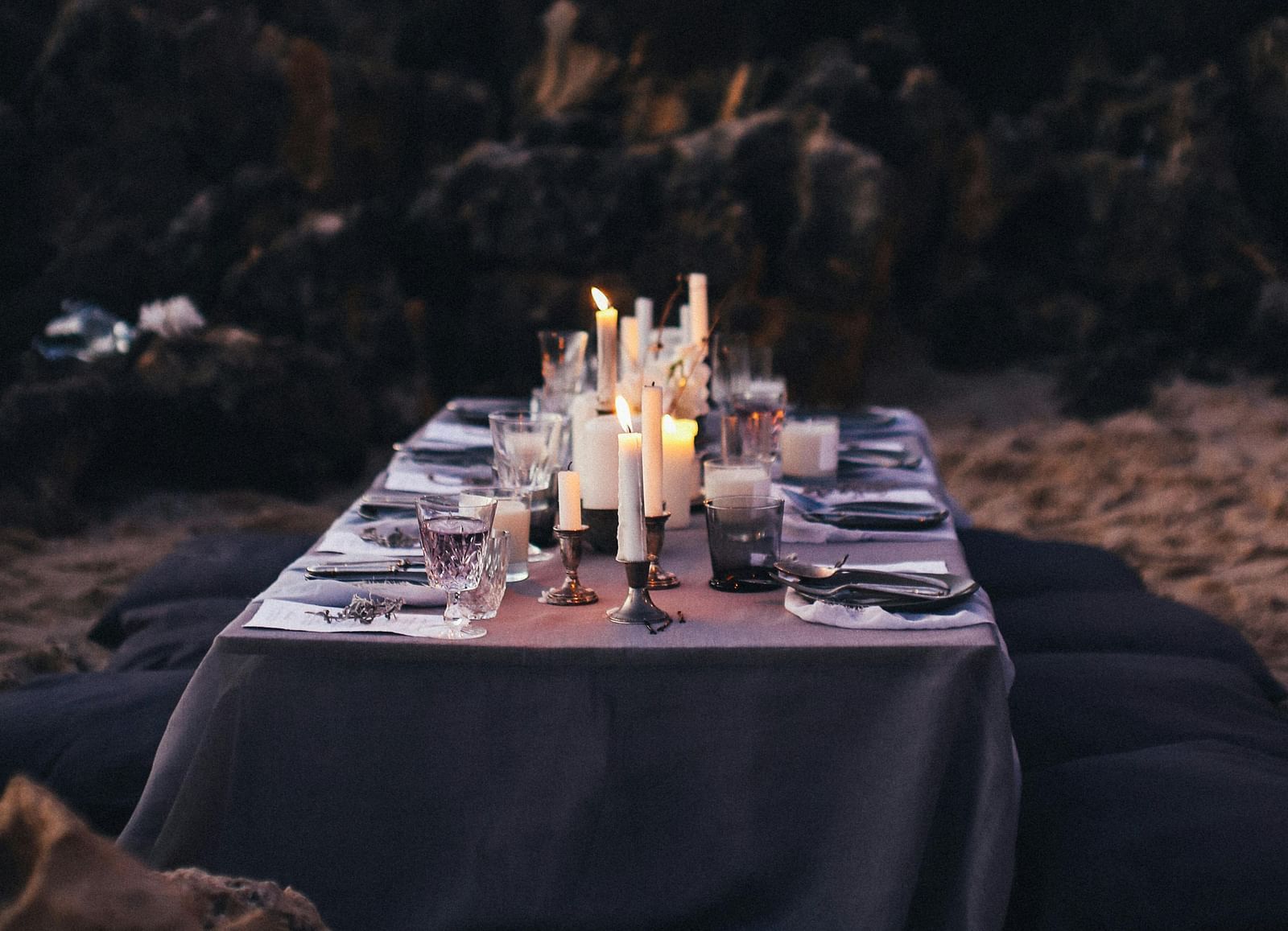 A dining arrangement by the beach with cutlery kept on a table and forest cover in the background.