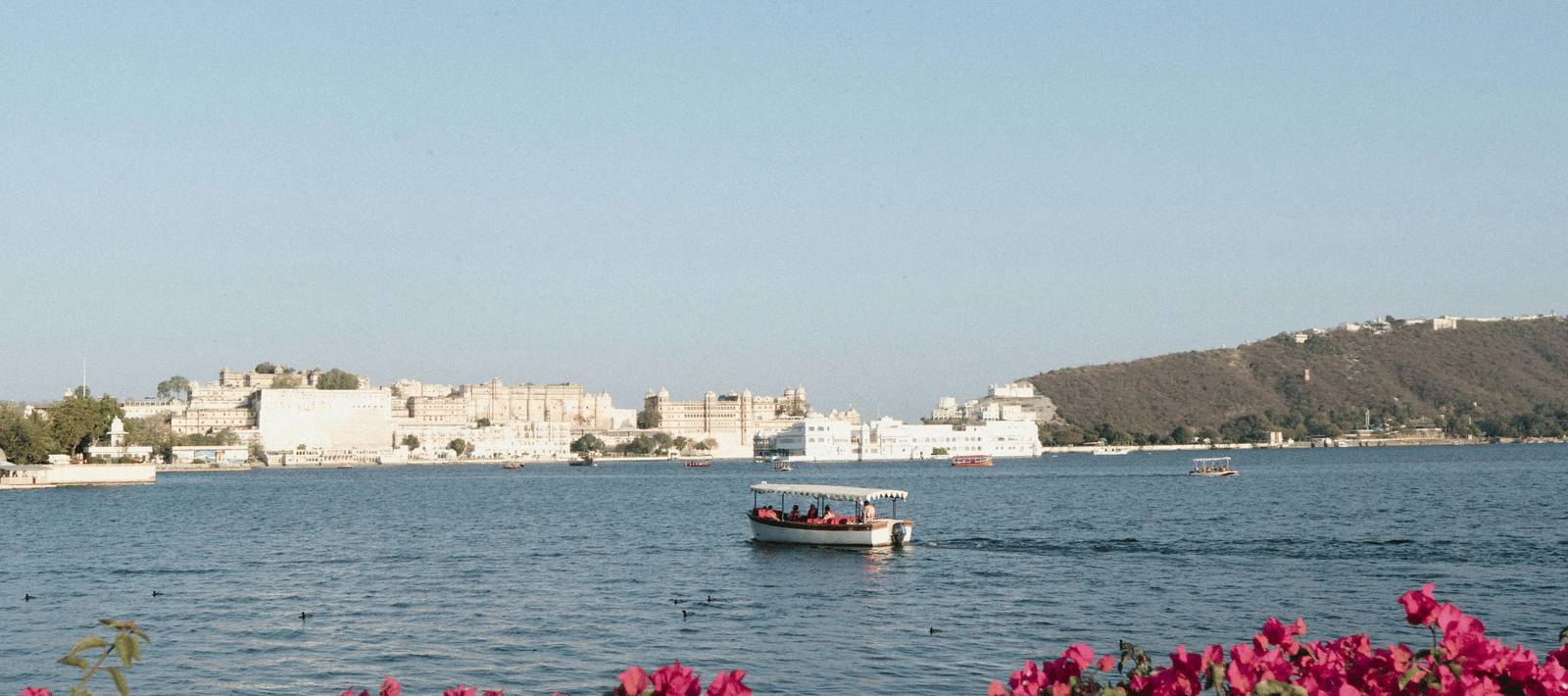 A boat sailing on the calm waters of Lake Pichola in Udaipur on a bright sunny day.