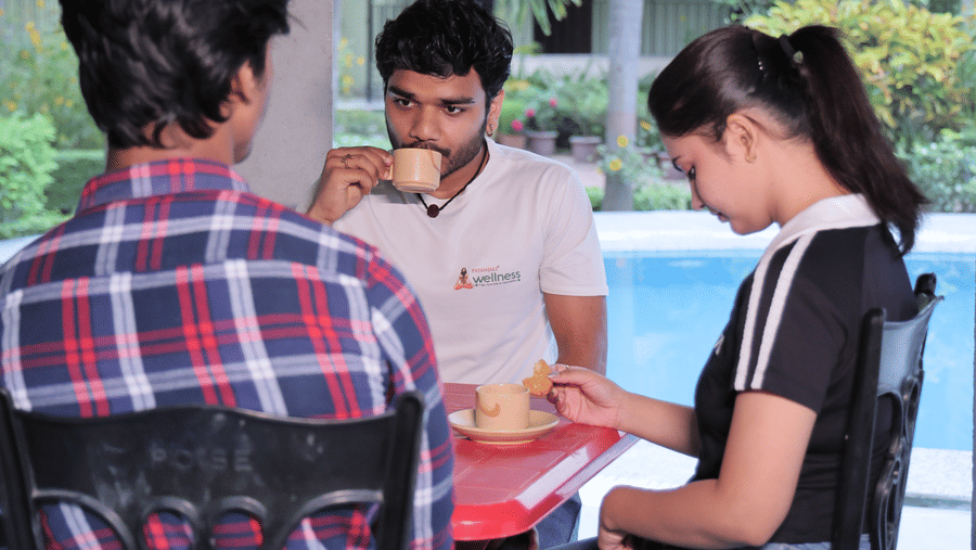 3 people sitting at an outdoor table under a thatched roof structure next to a pool at Shophori Wellness Retreat, Bolpur.