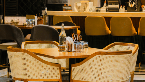 A dining area at Hotel Polo Towers, featuring a round table with chairs and a view of the bar.