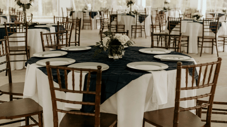 Elegant wooden chairs surround a round reception table dressed with white and navy linen.