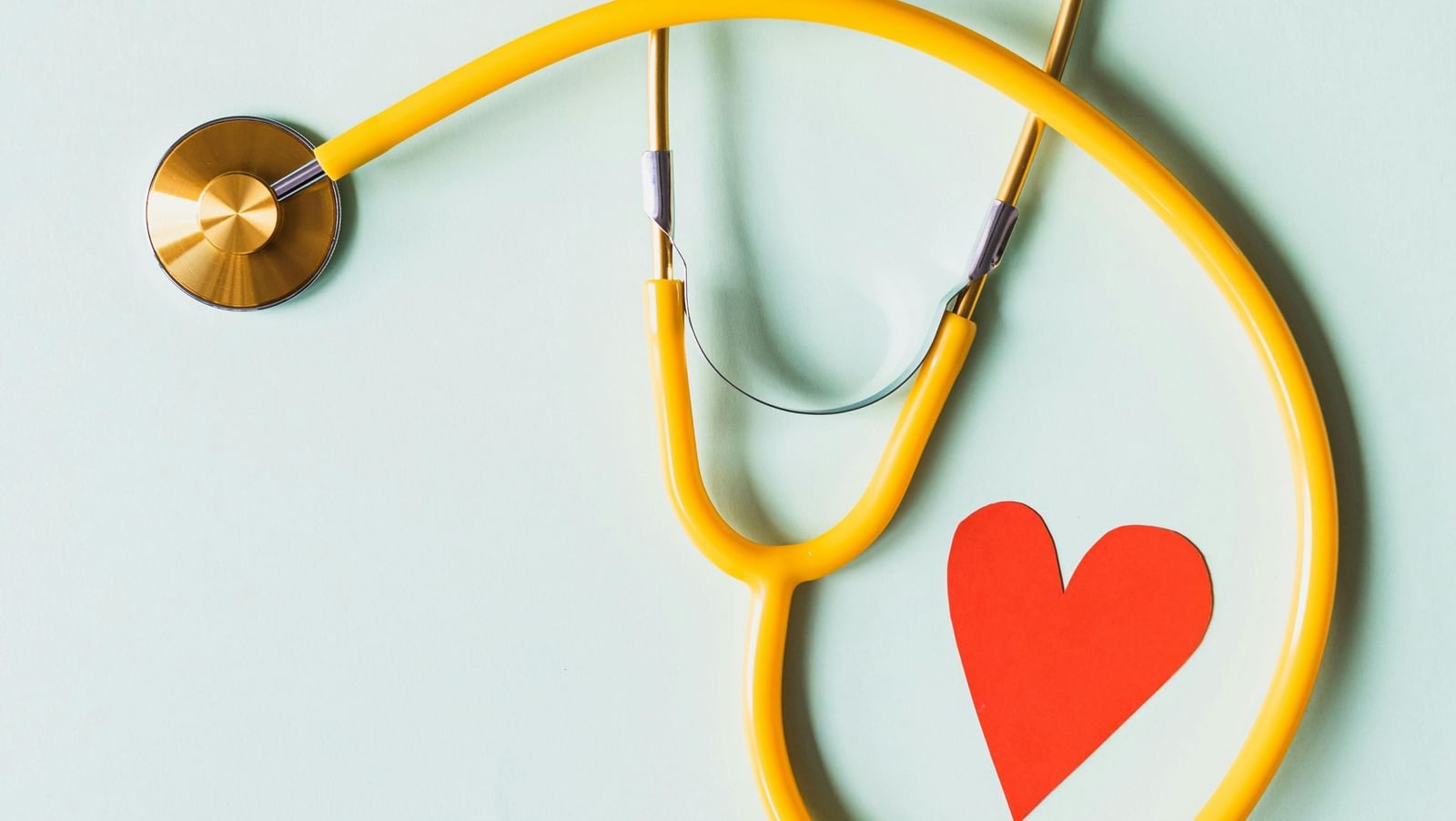 A stethoscope encircling a small red paper heart on a light background.