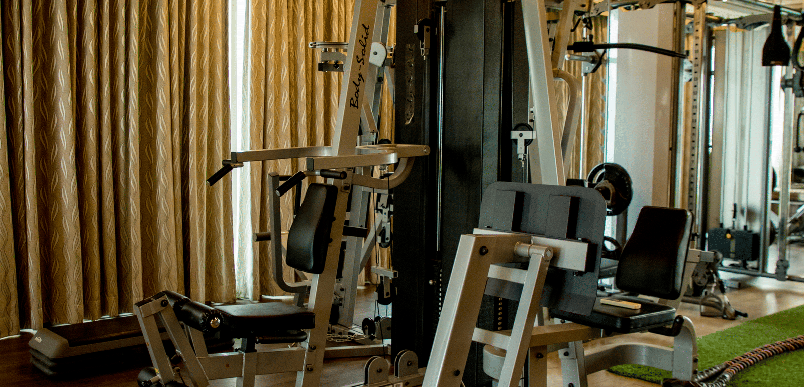 The fitness centre at the Benzz Park, Vellore, featuring a fitness equipment in dimly lit interiors.