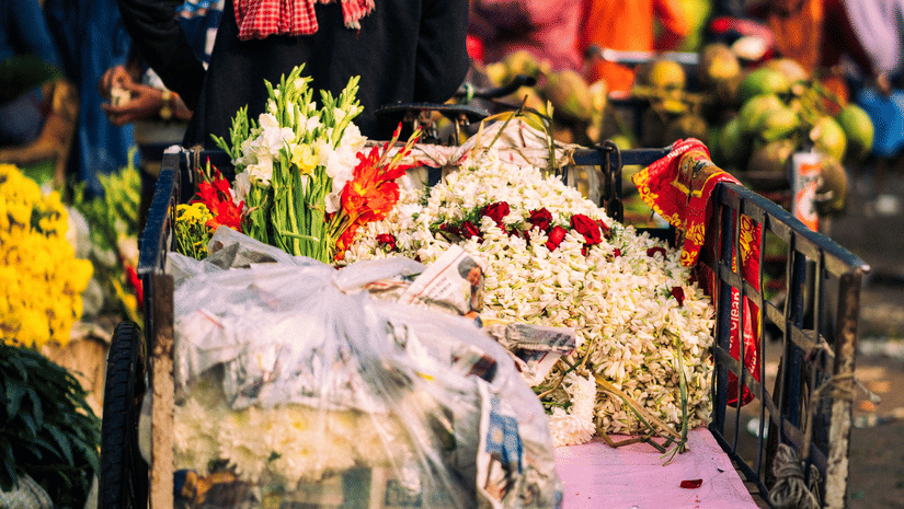 A person pulling a cart with various flowers on it in a market