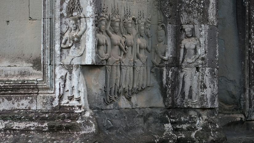 A close-up shot of weathered, gray stone architecture with intricate carvings, possibly depicting a section of an ancient temple.