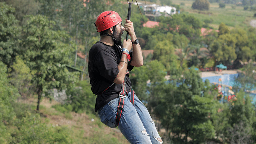 an image of  an individual performing zip line with lush green view at VITS Roccia Hill Resort & Adventure Park.