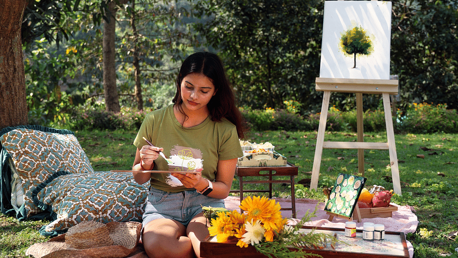 A woman sitting on a picnic mat painting at the Sylvan Retreat, Dehradun.
