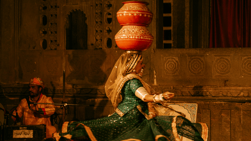 Traditional Rajasthani folk musician performing with a turban and string instrument inside a heritage setting.