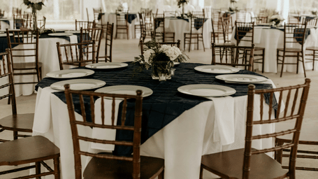 An elegant round dining table features a white cloth and a dark runner surrounded by classic wooden chairs.