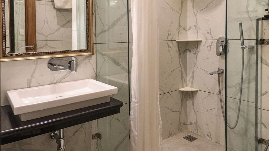 Spacious bathroom with a mirror above the washbasin and a glass panel separating the showering area | Panna Vilas Udaipur
