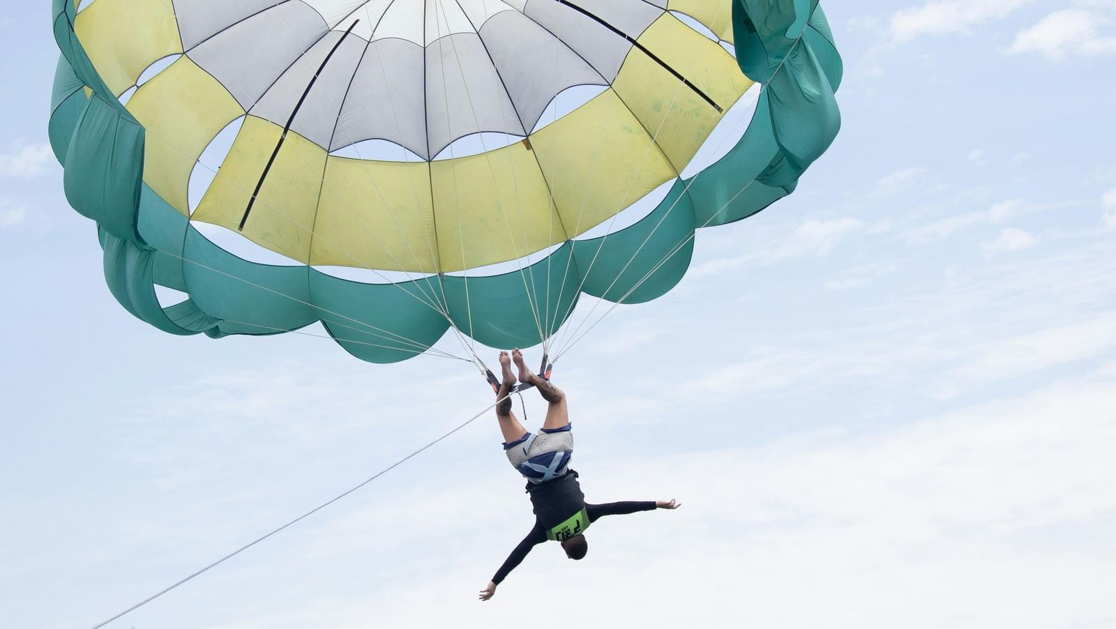 Person parasailing high above the waters with a colourful parachute open against a clear sky