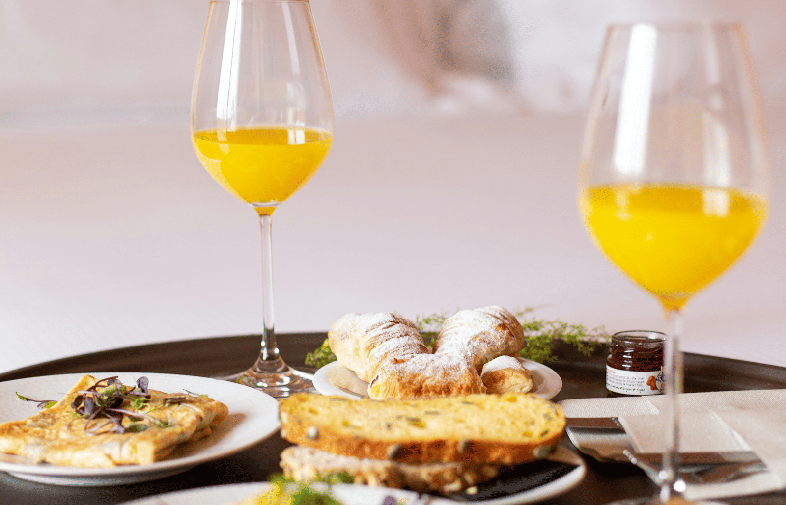 A room service breakfast tray with orange juice and an assortment of breakfast foods on a bed