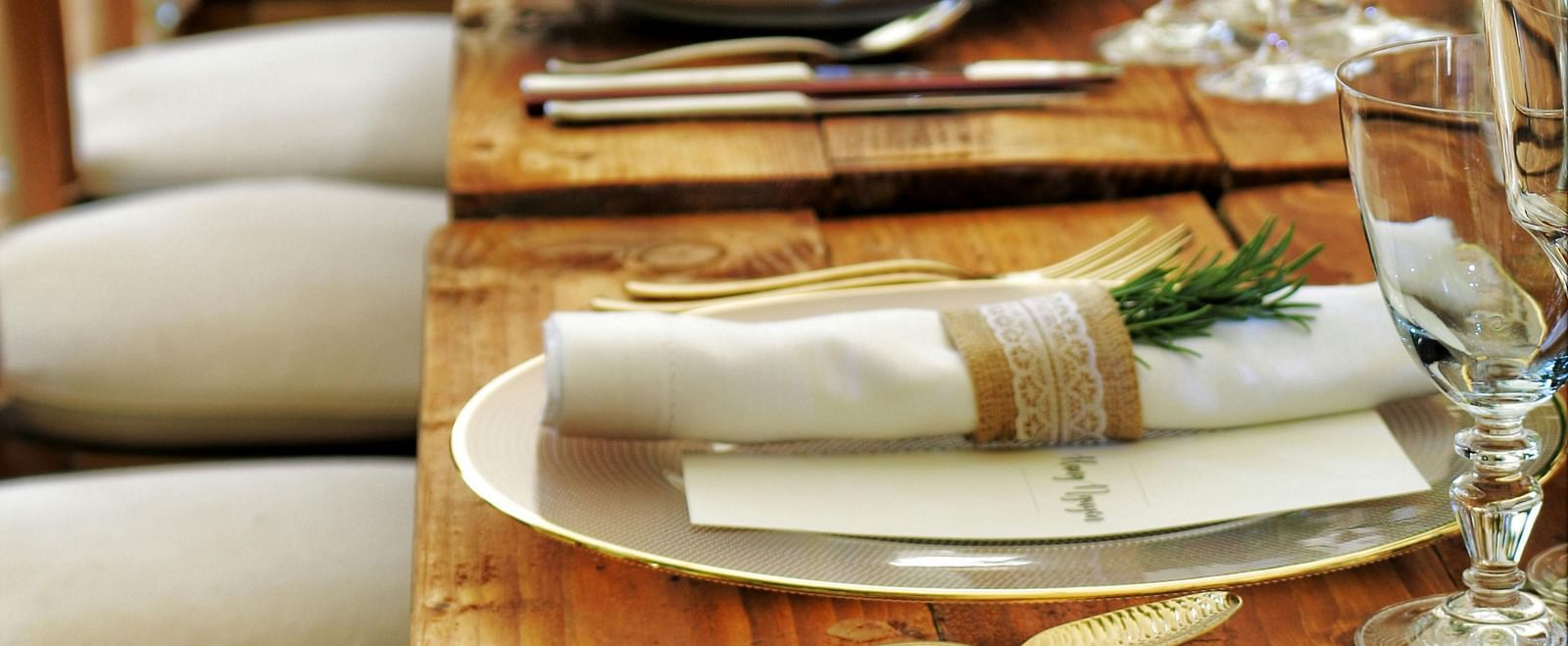 A long wooden table with beautifully set cutlery with small fern leaves in vases.