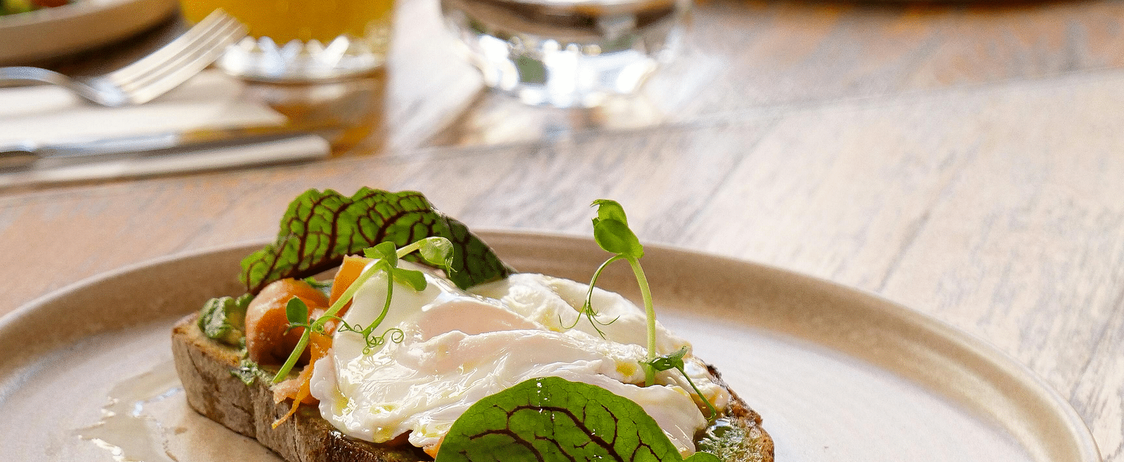 A toast with mayo placed on a plate and an orange juice in the background