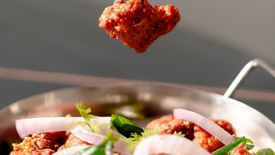 Tandoori chicken being picked up with a fork from a platter | Pravasa Hotel, Vijayapura