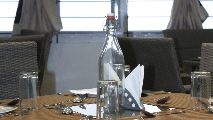 Close up of a dining table at the Spice and Slice Restaurant featuring cutlery and a glass water bottle in the middle of the table at WOW Naturefull Resorts, Yercaud.