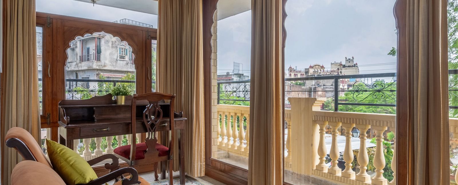 A room with ornate arched doorways leading to a balcony, lounge chairs, and a patterned rug | Dera Rawatsar, Jaipur