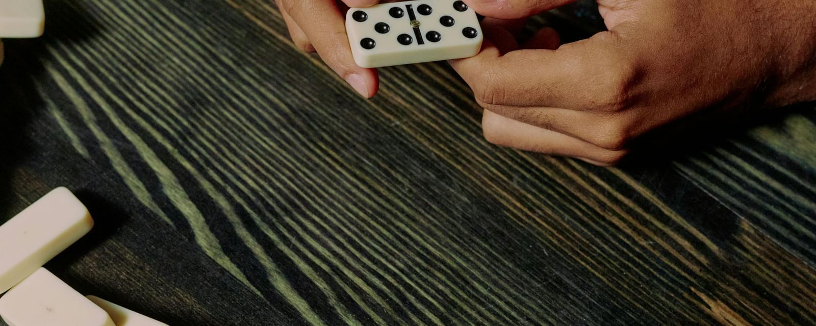 A hand placing domino pieces on a wooden table for an indoor game activity, symbolising fun and recreation at the homestay.
