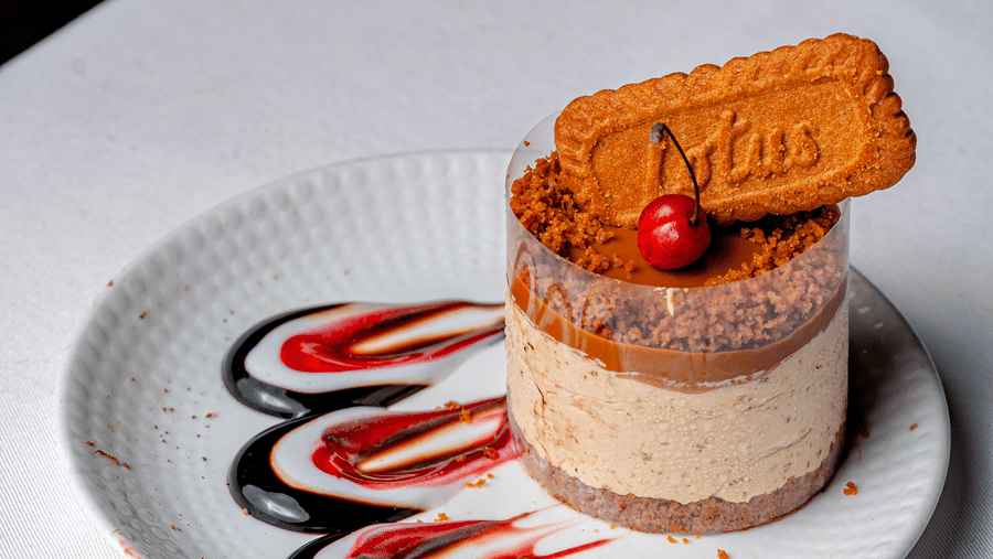 A Biscoff cheesecake garnished with a biscuit and red berry at Café Latte, located within Noor-Us-Sabah Palace, Bhopal, served on a decorated plate.