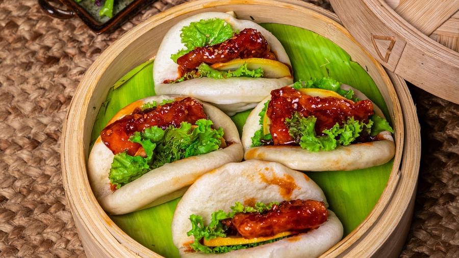 A bamboo steamer filled with buns stuffed with vibrant vegetables and proteins, accompanied by a tray of shredded purple cabbage and garnishes on a woven mat surface at The Hamuse Hotel, Kodaikanal.