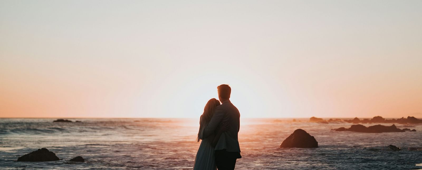 A couple hugging on a beach, against the backdrop of a serene sunset - Brewery Gulch Inn & Spa
