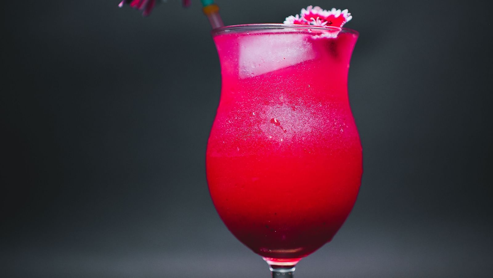 A vibrant pink mocktail served in a curvy glass with a decorative straw and a small paper umbrella, set against a dark background at D Café in Dip Holidays.