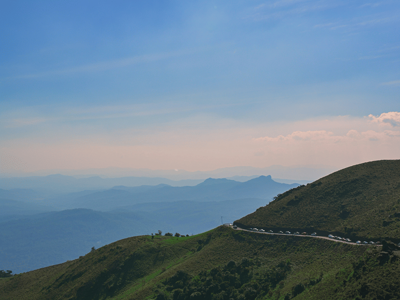 A winding mountain road cutting across a lush green hill under a bright sun