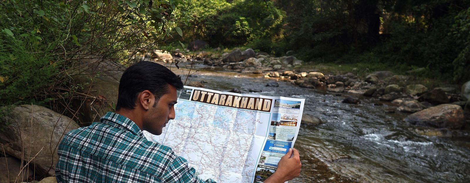 A man reading a map sitting near the stream at A man flying a kite at The Sylvan Retreat, Dehradun.