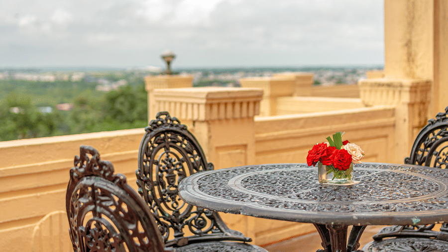 A close-up shot of the private terrace of the Crown Club Suite at Noor-Us-Sabah Palace, showing ornate black metal chairs overlooking the lush landscape and lake.