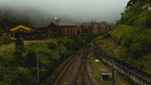 A railway track running through hills with greenery and mist around.