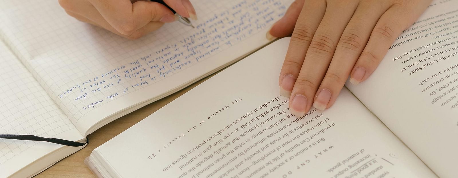 image of a person referring a book and writing something in a notebook with pen