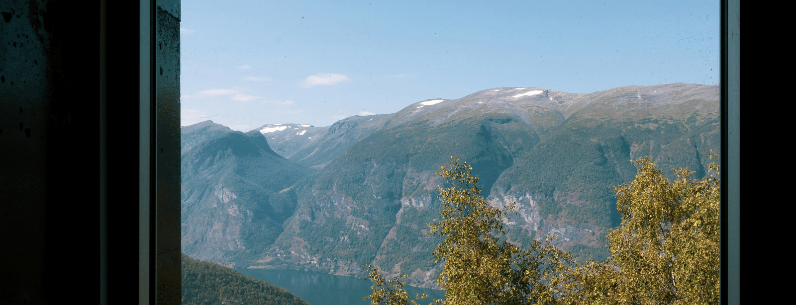A bright view of a forested valley and distant, snow-dusted mountain tops framed by a dark, square window.