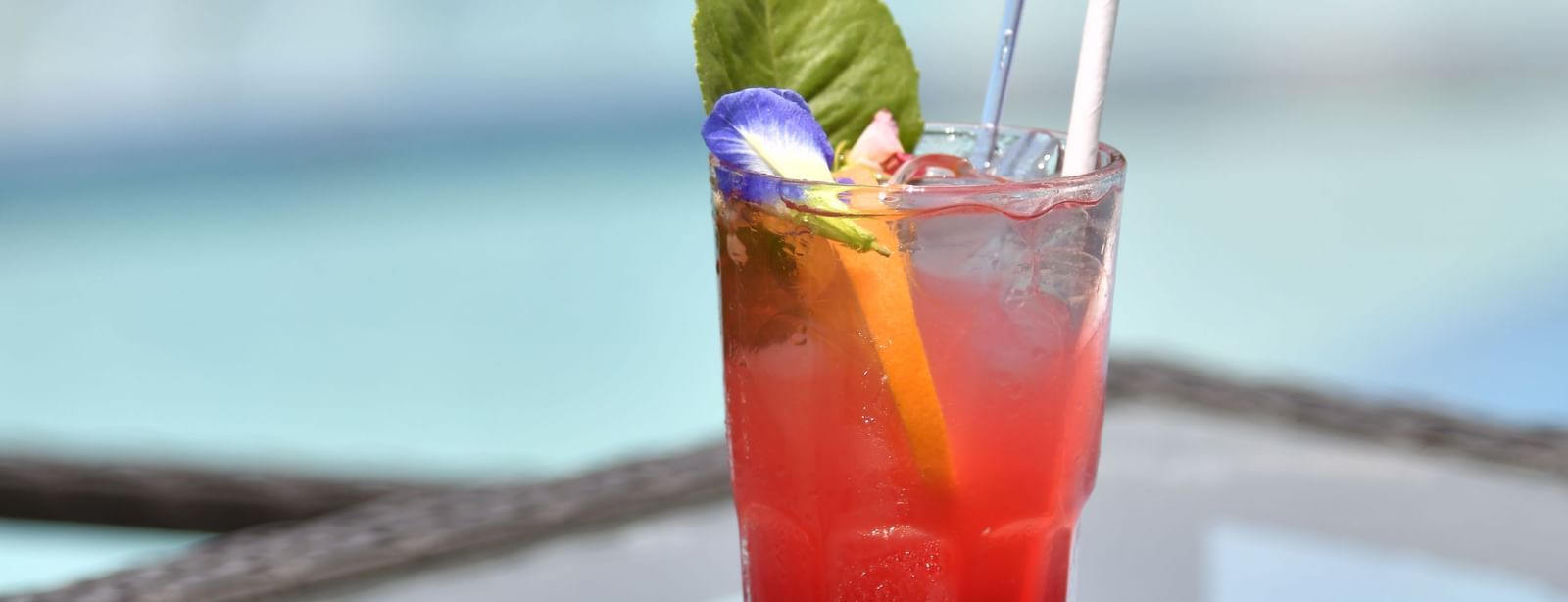 A red drink with a garnish in a glass , placed on a poolside table, at Vedic Village Spa Resort.