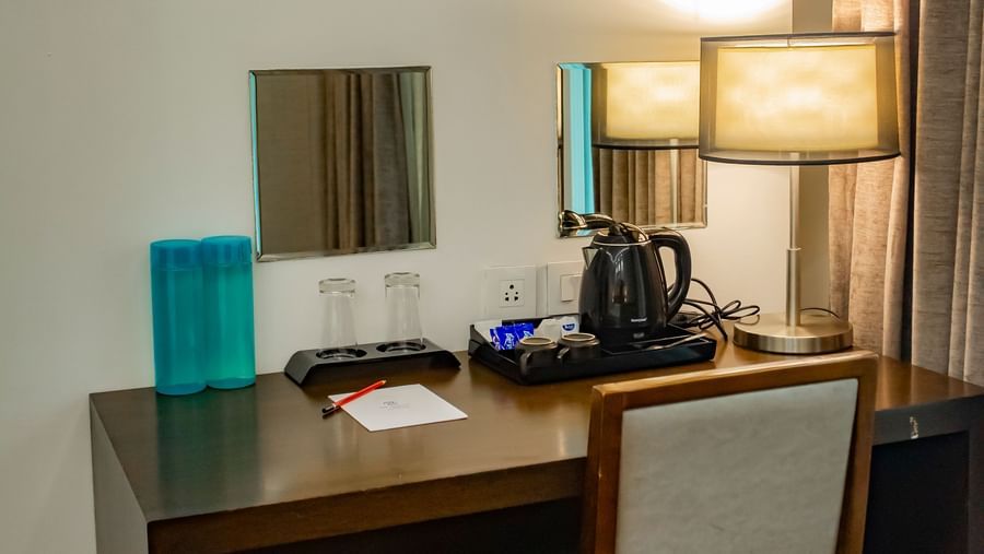 A compact workspace with a wooden desk, chair, table lamp, and wall mirrors at The Hamuse Hotel, Kodaikanal.