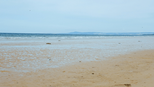 An overview of an empty beach with golden sands and water in the distance.