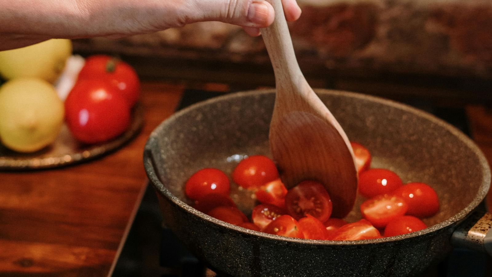 A hand holding a ladle sauteing tomatoes placed on a pan.