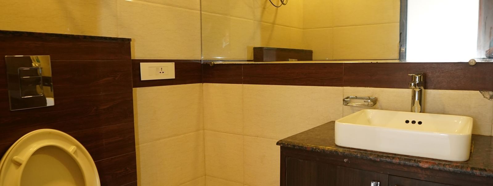 Bathroom at Hotel Dreamland, Chandigarh with Western commode, wall-mounted water heater, mirror and sink with storage shelf below.