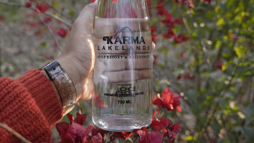 A person holding a water bottle in front of red flowers - Karma Lakelands.
