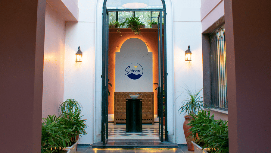 Exterior view of Sierra's arched entrance surrounded by plants, with the logo above and a pebbled pathway leading to the door.