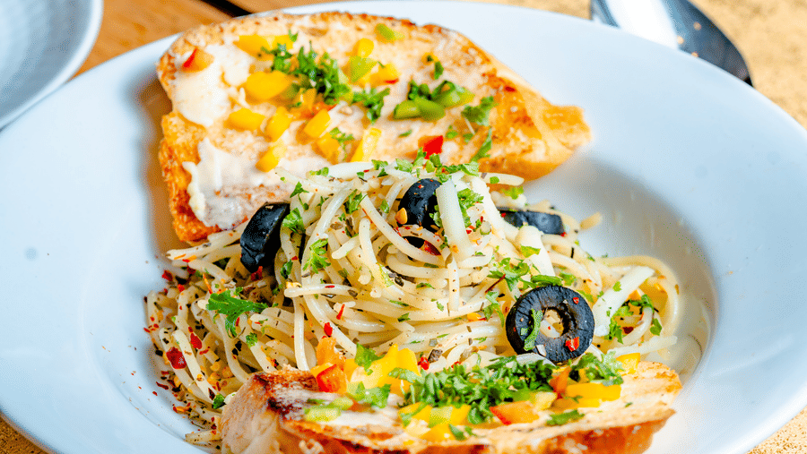 Creamy pasta served on toasted bread with black olives at Marble Arch, located within Noor-Us-Sabah Palace, Bhopal, presented on a set dining table.