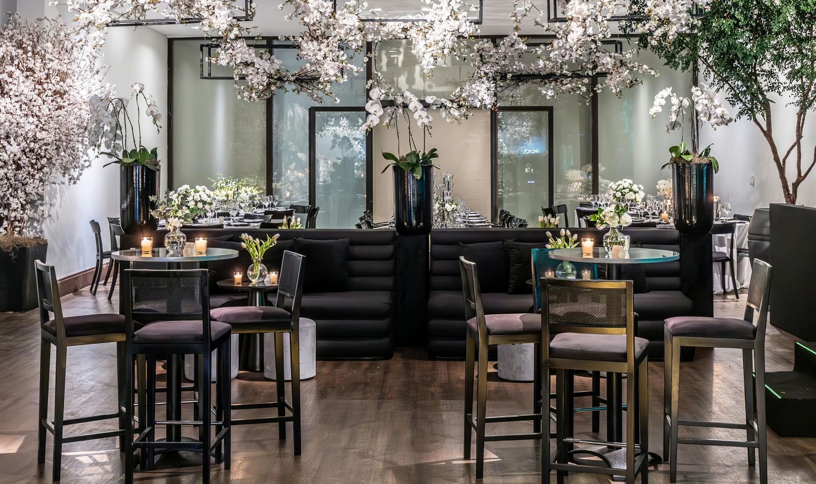 Brightly lit indoor event space with small tables, chairs, and floral decorations.
