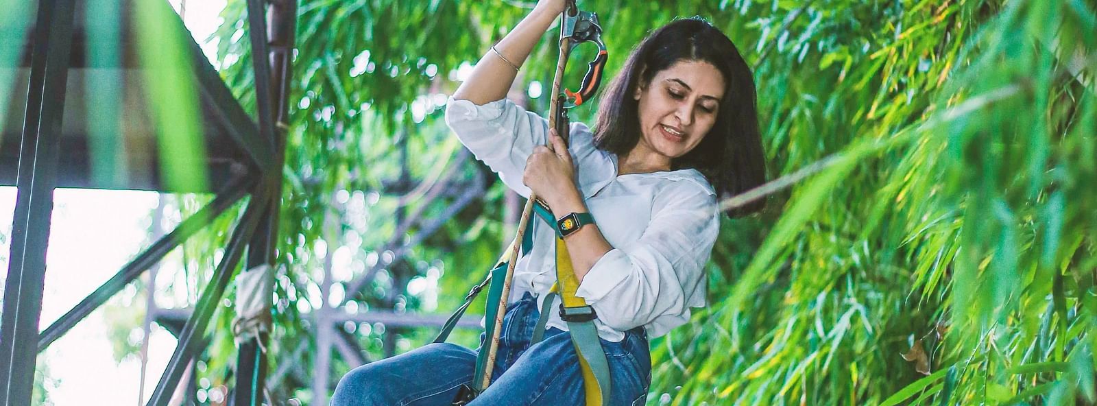 A girl climbing on a rope structure in a lush green area.