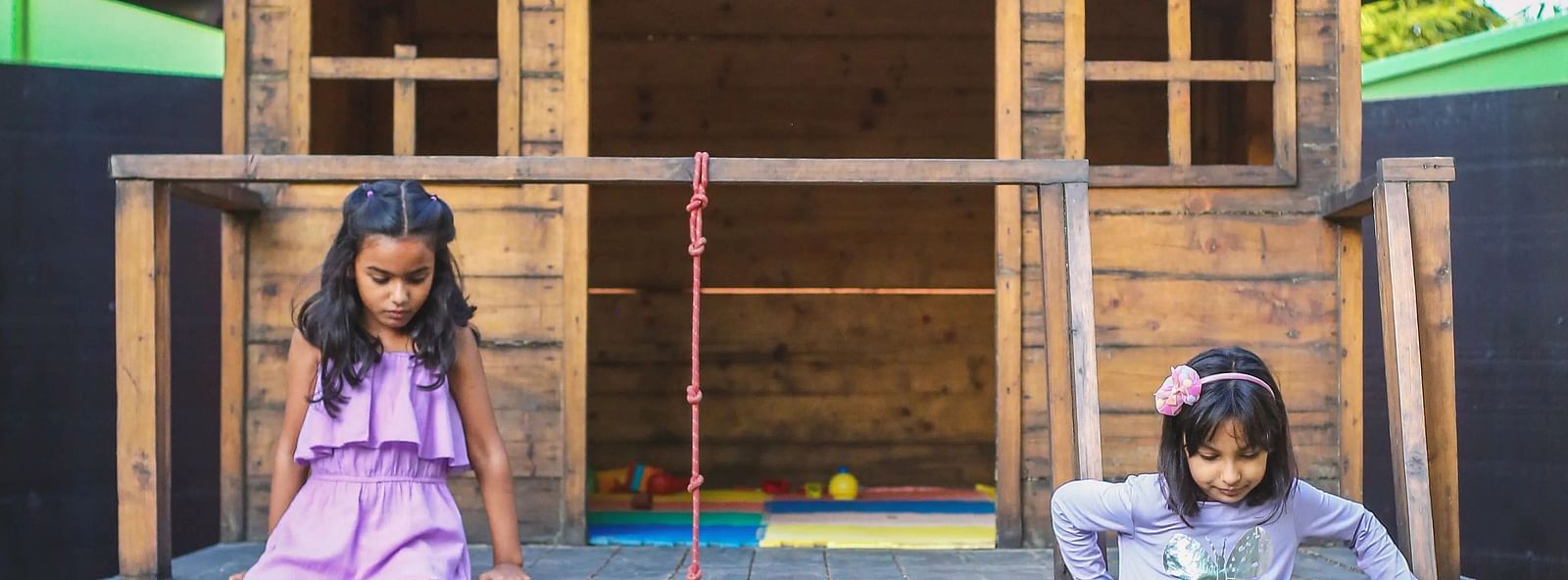 Two kids playing in front of a small wooden house.
