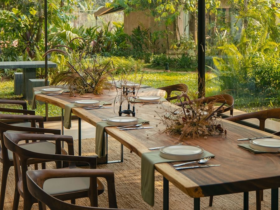 Elegant dining table setup with garden views inside the glass pavilion at Villa Moira Goa